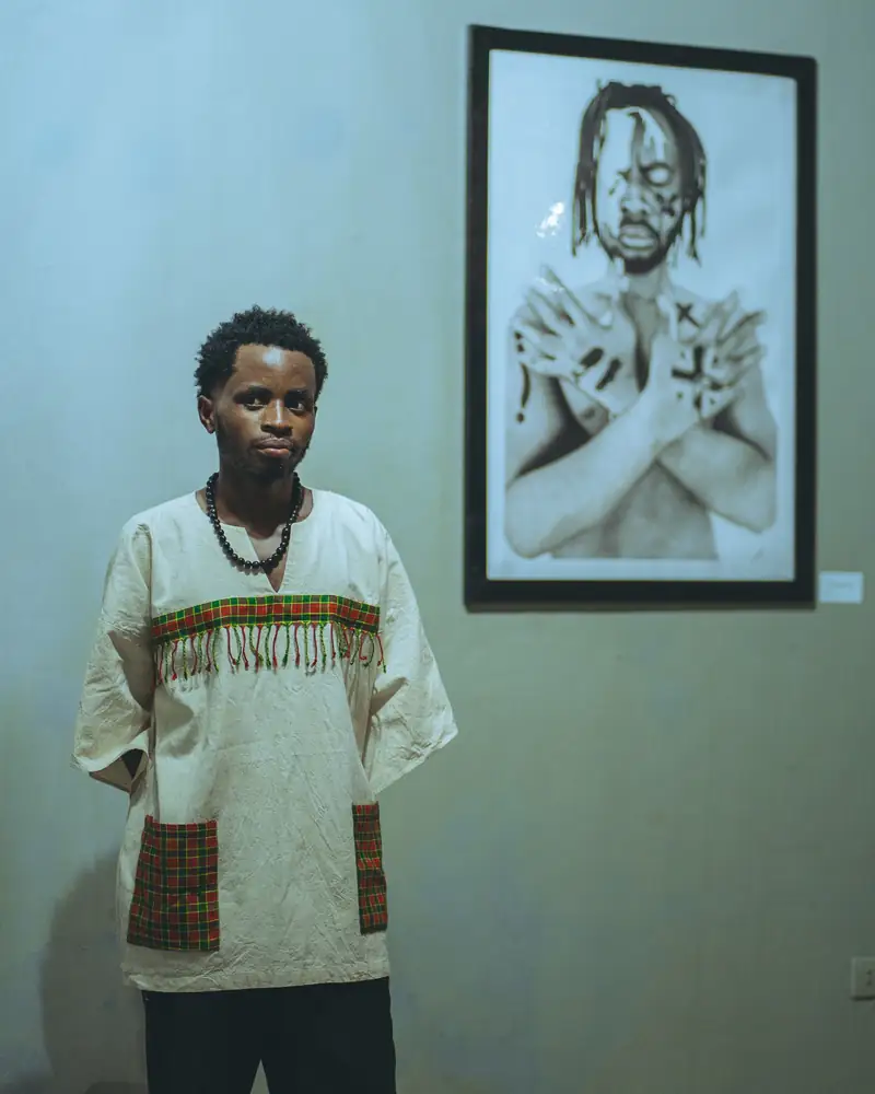 Un jeune homme pose à côté de son dessin encadré, exposition « Résonance », avril 2025
